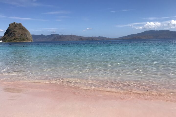 Beach with pink sand and turquoise water with volcanic islands in background
